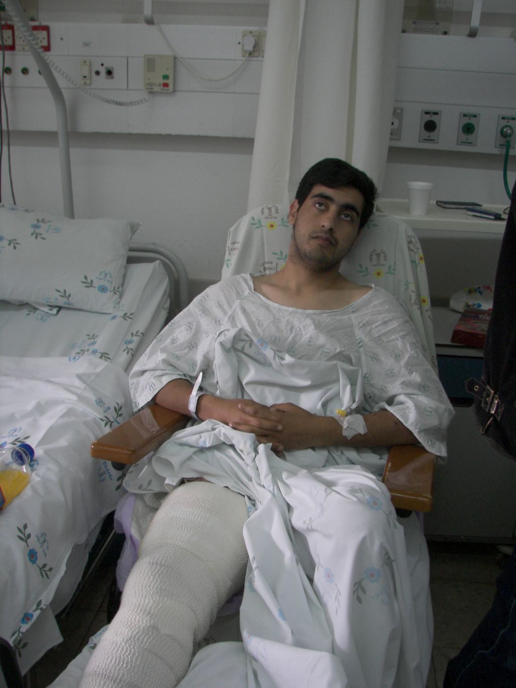 Un joven serio, herido, piernas vendadas, en cama de hospital