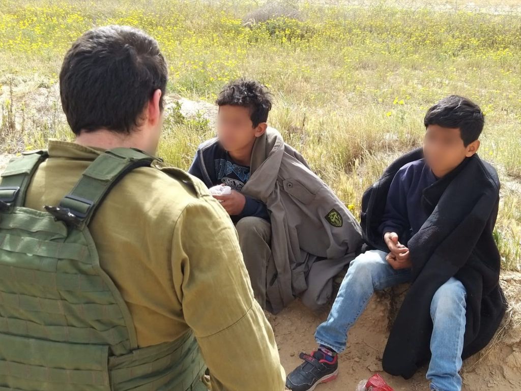 Dos niños palestinos sentados hablando con un rastreador del ejército israeli sobre por qué habían curzado la frontera