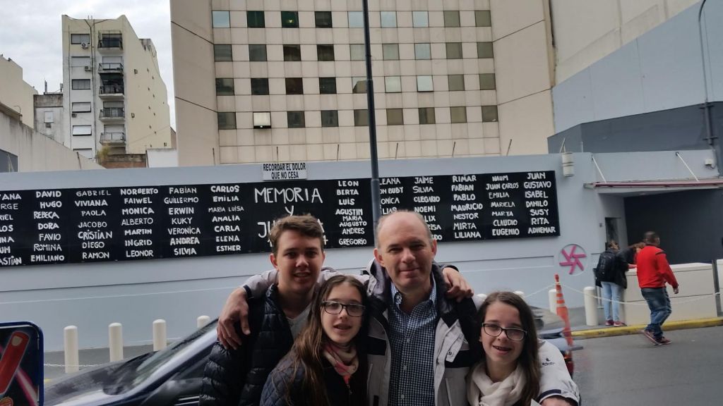 Javier y sus hijos, en el 2017, a la entrada del nuevo edificio de AMIA. Detrás, el muro con los nombres de las víctimas, entre ellos, numerosos de sus compañeros de trabajo.