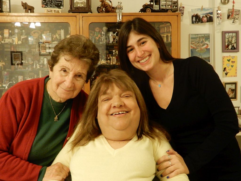 Becky Sabah, su tía Raquel Hadjez y una de sus sobrinas, en Kfar Saba, Israel Tres mujeres juntas. Becky Sabah, de buzo amarillo, en silla de ruedas que no se ve, a su izquierda su tía Raquel y a la derecha una de sus sobrinas, ambas apoyándose en la cabeza de Becky en señal de cariño