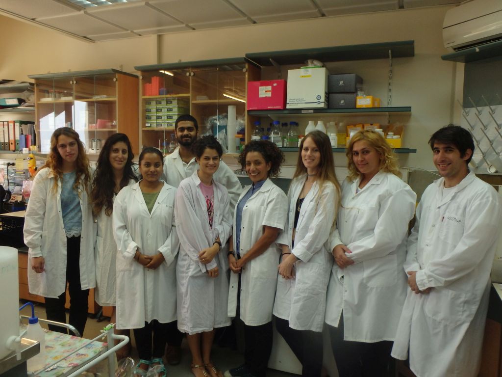 Un grupo de pie en un laboratorio, todos de túnica blanca, carmit levy en el medio