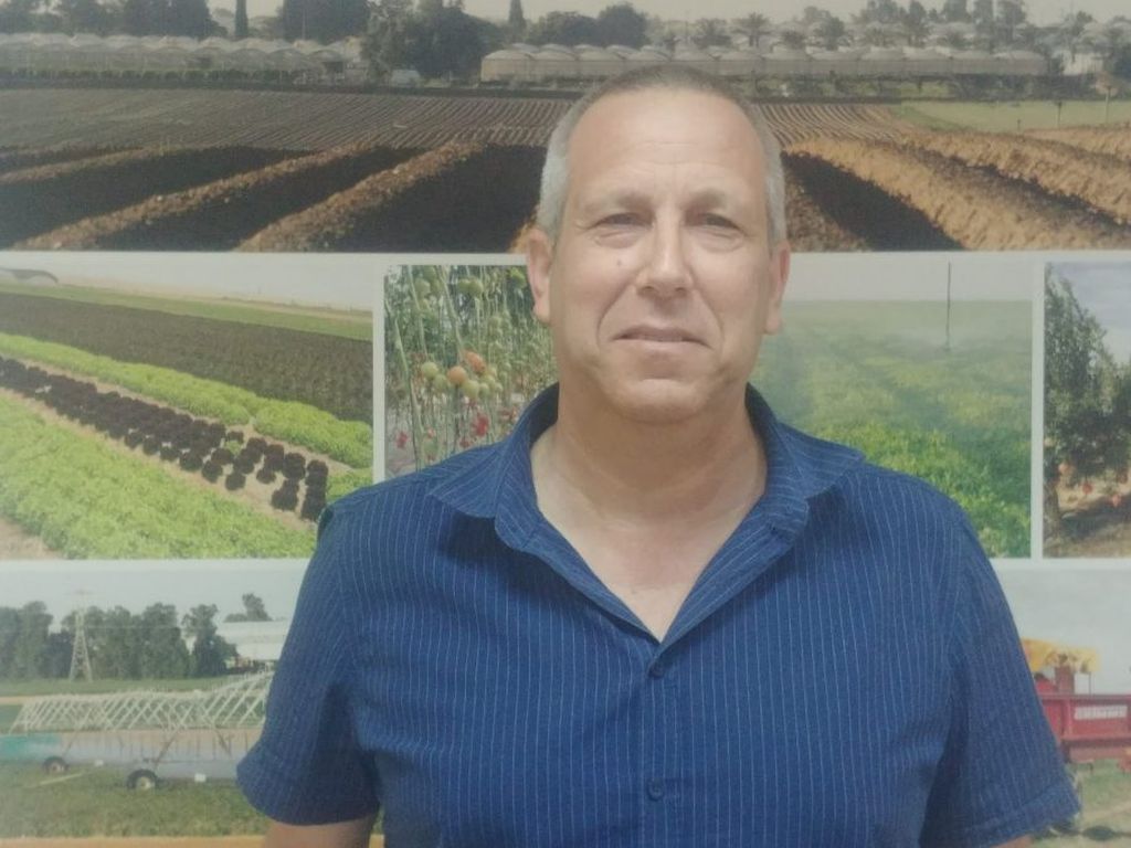 Gadi Yarkoni, de remera azul, foto medio cuerpo, de fondo fotos de cultivos