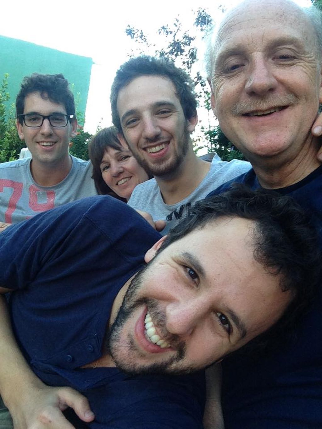 Un joven de barba, sonriente, al frente de la foto, adelante de sus hermanos y padres