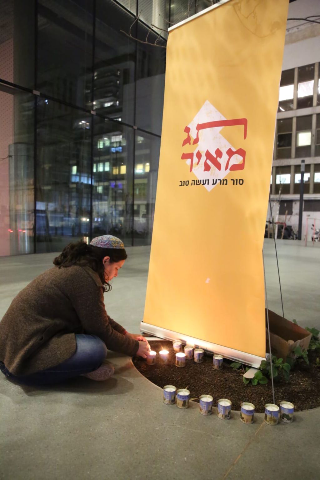 Una participante judía en la actividad de Tag Meir, agachada frente a un cartel con el nombre de la organización, enciende una vela recordatoria
