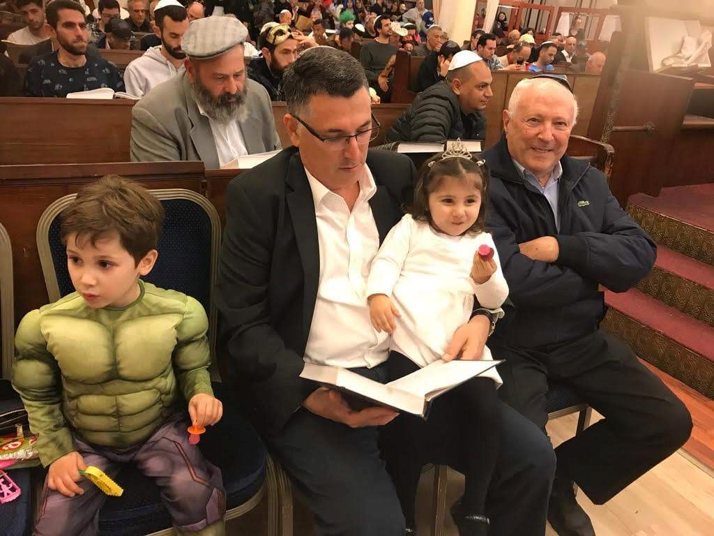 En el Beit HaKneset en Purim, leyendo Megilat Esther con su padre y sus hijos pequeños
