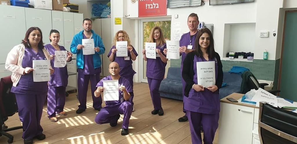 Personal médico de judíos y árabes, en uno  de los hospitales del norte de Israel, pidiendo con carteles en hebreo y árabe a la ciudadanía : "Nosotros estamos aquí, por ustedes. Quédense en casa, por nosotros"