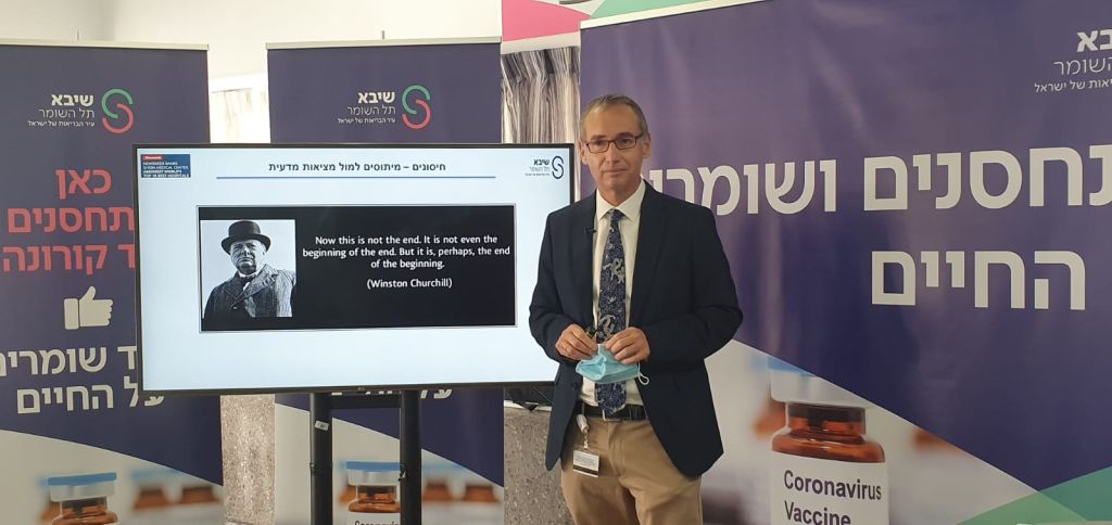 El Profesor Afek junto al centro de vacunación en su hospital. De fondo, un poster con un pensamiento de Winston Churchill apropiado a la situación: “Ahora esto no es el fin. No es ni siquiera el comienzo del fin. Pero es, quizas, el fin del comienzo”