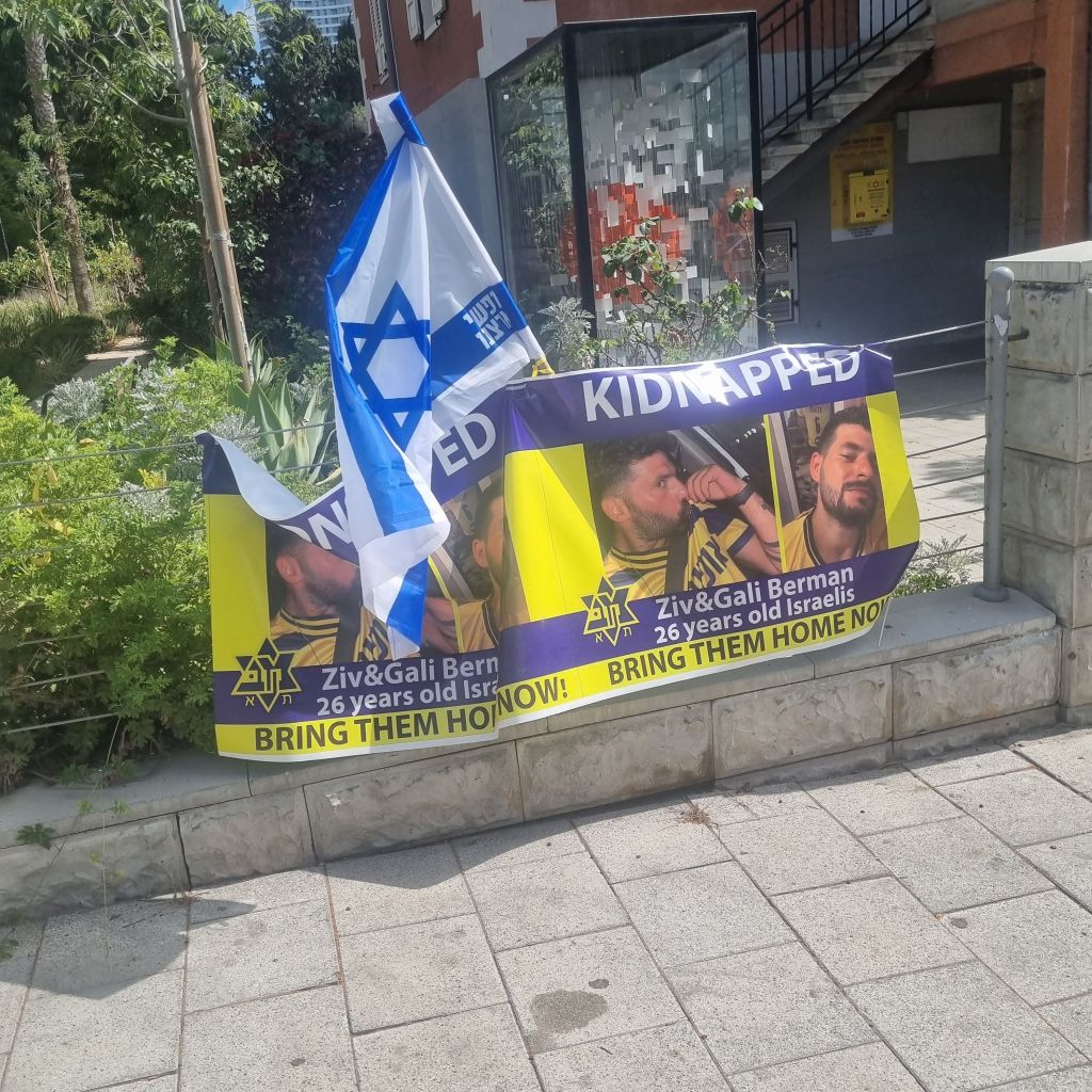 En una esquina de Tel Aviv, un recordatorio y homenaje que se ve en muchos puntos más, por todos los secuestrados. Aquí, por los mellizos Gali y Ziv Berman del kibutz Kfar Aza, con las banderas del cuadro que aman, Macabi Tel Aviv