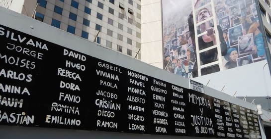 La pared contigua a la entrada a la AMIA en la calle Pasteur tal cual se la ve hoy, con los nombres de los asesinados en el atentado, y la pared pintada del interior.