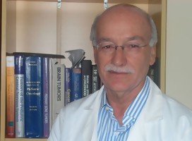 El oncólogo infantil Dr Ney Castillo, de túnica blanca, foto medio cuerpo, libros de su biblioteca de fondo