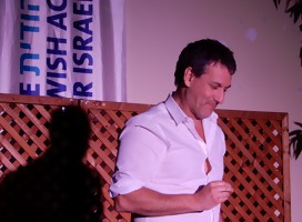 Franklin Rodríguez, de camisa blanca, medio cuerpo, en Raananam sobre el escenario, de fondo cartel en el que dice Israel