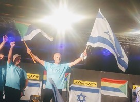 Amal Assad con dos banderas, la de Israel y la de los drusos, una en cada mano, levantándolas en alto.A su izquierda, otro de los participantes en el liderazgo de la protesta drusa. De fondo, en el estado del acto en la plaza Rabin banderas de israel y de