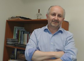 Pablo da Silveira, de brazos cruzados, mirando de fondo a la cámara. De fondo, una bibilioteca con libros.