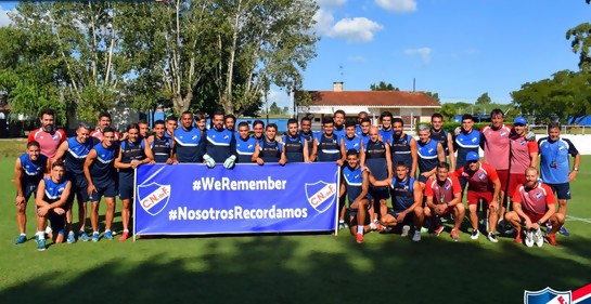 El plantel completo de Nacional en Primera División y el Equipo Técnico, con la pancarta que dice We Remember y Nosotros Recordamos, de fondo azul, con el escudo de Nacional a ambos costados. Letras blancas.