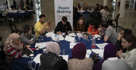 Jóvenes sentados alrededor de una mesa, tanto judíos como palestinos. De fondo, un cartel que dice Peace Making