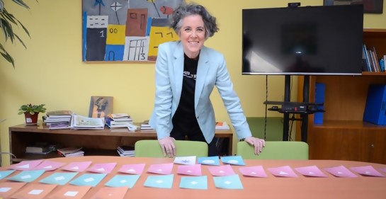 Mariana, sonriente, de pie junto a una mesa llena de piezas de colores