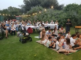 Adultos y jóves en una celebración comunitaria, algunos sentados en sillas y otros en el césped