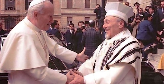 El Papa, de blanco y el rabino, cubierto con el Talit, extendiendo mutuamente los brazos sonriendo ambos y tomándose las manos