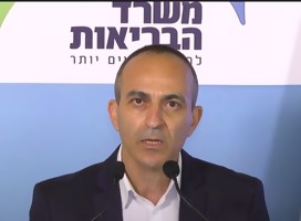 El Profesor Roni Gamzo hablando ante cámaras, entre dos banderas de Israel. De fondo, un banner del MSP de Israel