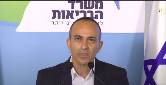 El Profesor Roni Gamzo hablando ante cámaras, entre dos banderas de Israel. De fondo, un banner del MSP de Israel