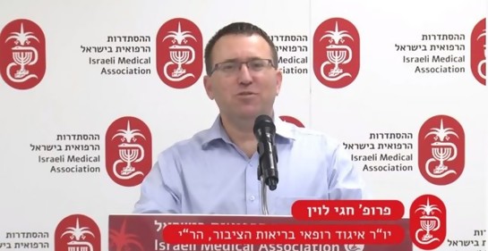 Prof Levine en una conferencia de la Asociación médica de Israel. En el podio. De fondo, logo de la asociación.
