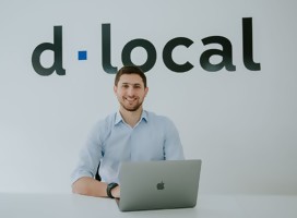 Jacobo Singer junto a su laptop, de fondo el logo de la empresa d.local