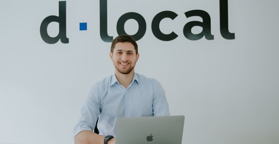 Jacobo Singer junto a su laptop, de fondo el logo de la empresa d.local