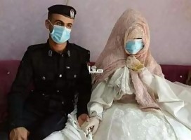 Un hombre de uniforme, con barbijo, junto a su novia, a la que por el velo que le cubre la cabeza y el tapabocas no se le ve la cara, de la mano, en su boda