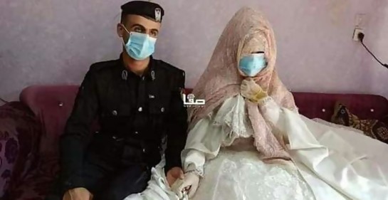 Un hombre de uniforme, con barbijo, junto a su novia, a la que por el velo que le cubre la cabeza y el tapabocas no se le ve la cara, de la mano, en su boda