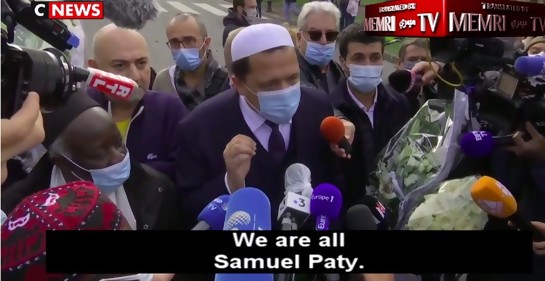 ImamChalgoumi, con tapabocas, hablando a la prensa, rodeado de micrófonos y mucha gente