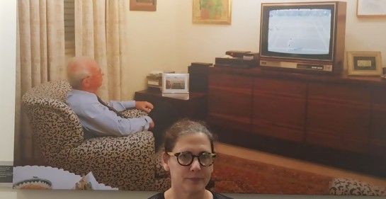 Una mujer de negro, de lentes, mirando a la cámara. De fondo, una foto gigante de Itzjak Rabin en su sala de estar