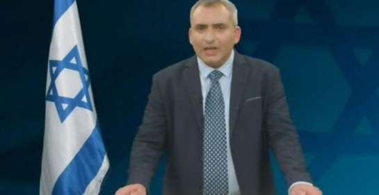 El ministro Elkin hablando, a su lado, una bandera de Israel